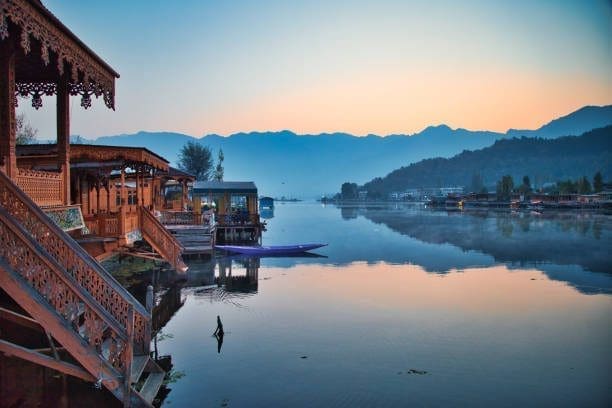 Houseboats reflect in a tranquil lake, mountains in the distance on the Srinagar to Gulmarg dawn
