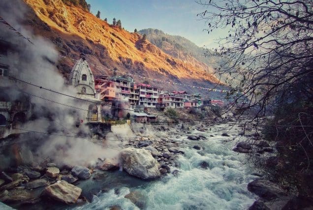 Steam rising from Manikaran hot springs in Kasol with riverside view, part of the best travel packages in India.