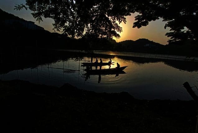 Silhouette of people boating at sunset on a calm lake – Guwahati Trip